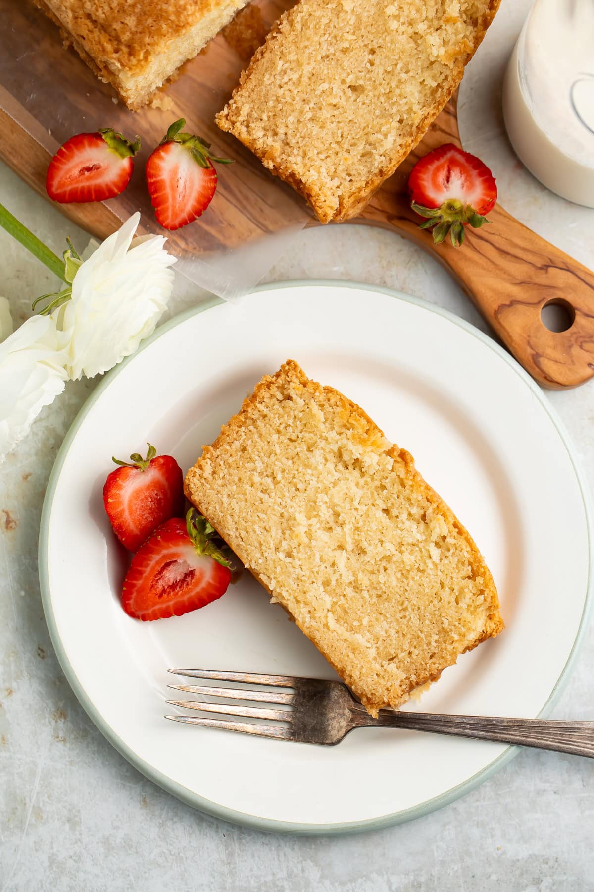 Slice of vegan pound cake on a white plate with a fork and a halved strawberry.