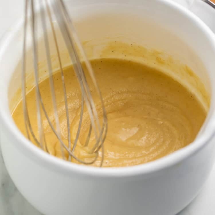 Whisk suspended against a finished white saucepan of gluten free roux.