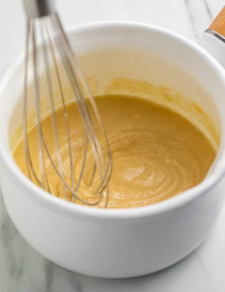 Whisk suspended against a finished white saucepan of gluten free roux.