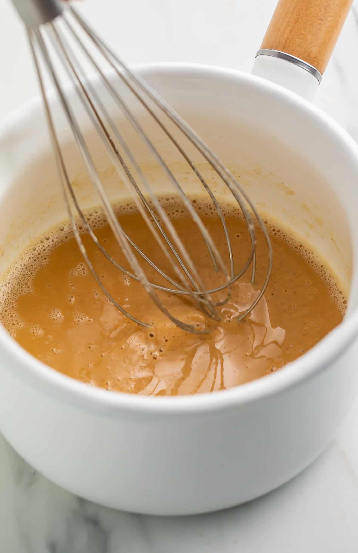 Gluten free roux mixture being whisked in a white saucepan.