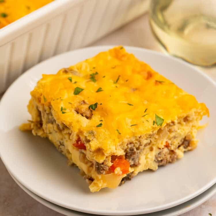 Slice of egg bake on a white plate with the casserole in the background in a white dish.
