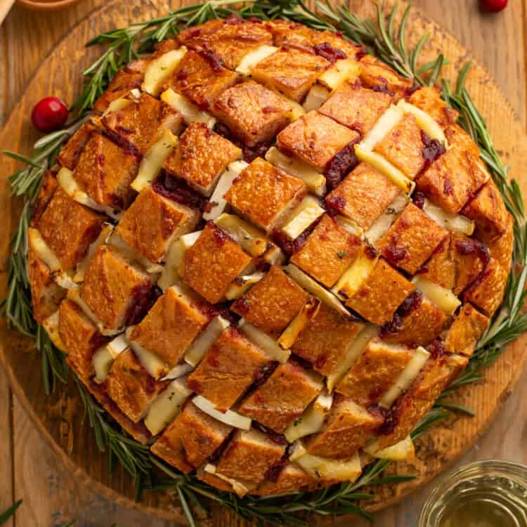 Top down view of a cranberry brie pull apart bread on a wooden board garnished with rosemary sprigs around it like a wreath.