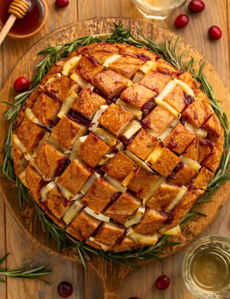 Top down view of a cranberry brie pull apart bread on a wooden board garnished with rosemary sprigs around it like a wreath.