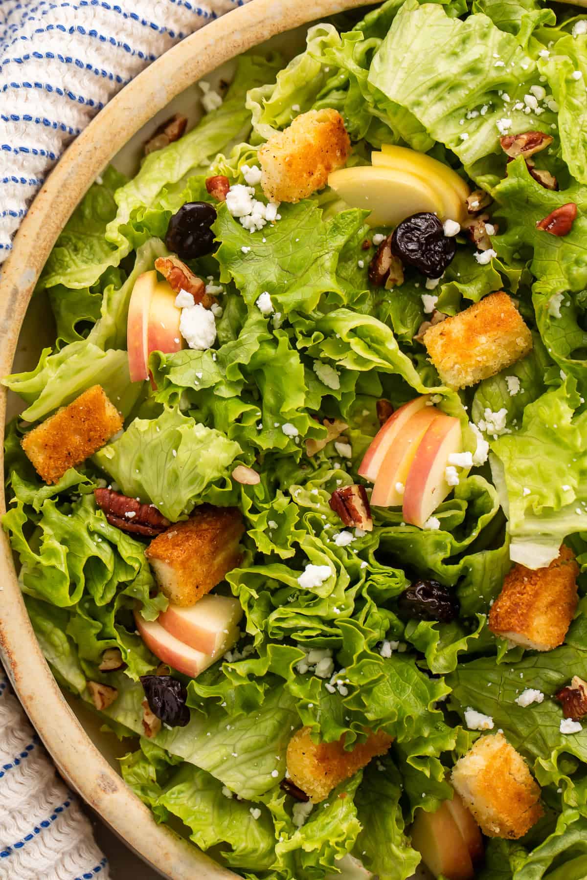 Close up of a salad in a wooden bowl with sliced apples and homemade gluten free croutons.