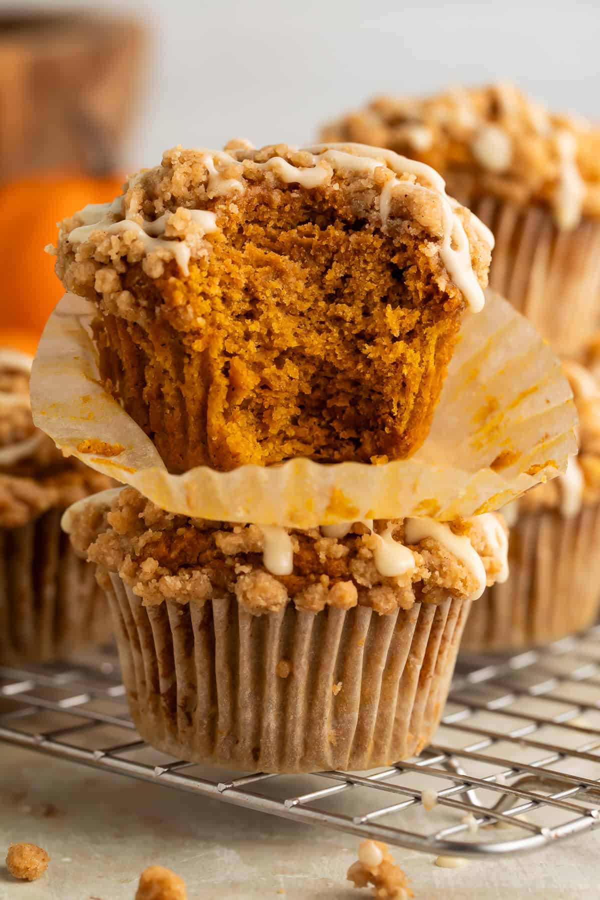 Pumpkin muffin with a bite missing stacked on top of another muffin on a cooling rack.