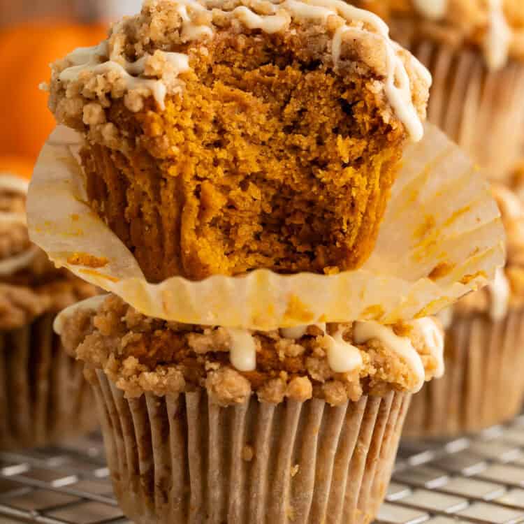 Two pumpkin muffins stacked on top of each other. A bite has been taken out of the top one to show the inside.
