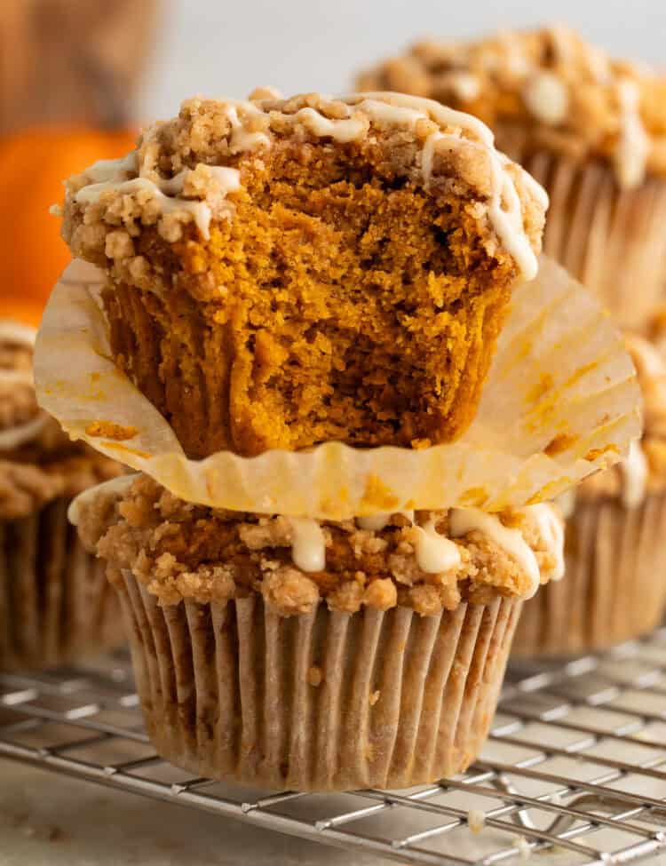 Two pumpkin muffins stacked on top of each other. A bite has been taken out of the top one to show the inside.