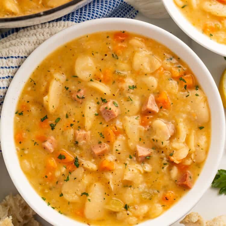 Close up of a white bowl of lima bean soup with another bowl and the casserole pot visible off to the side.