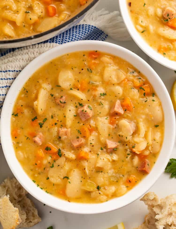 Close up of a white bowl of lima bean soup with another bowl and the casserole pot visible off to the side.