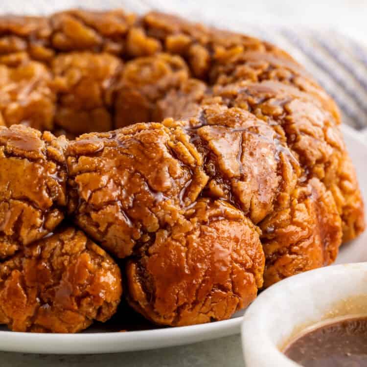Side on view of monkey bread on a white plate with a white bowl of caramel off to one side.