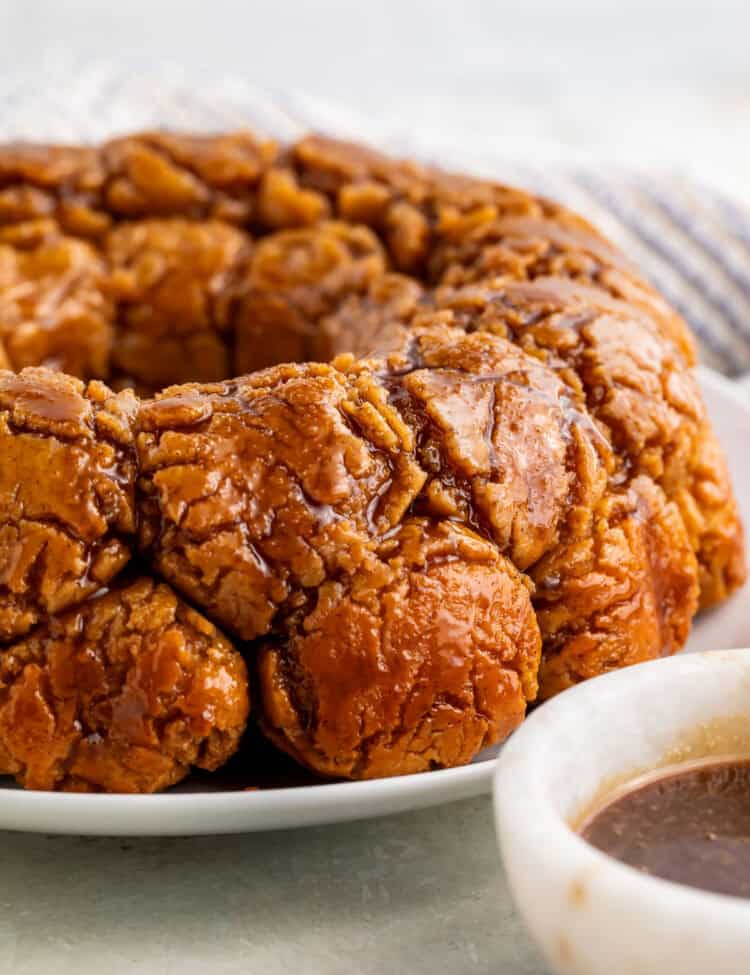 Side on view of monkey bread on a white plate with a white bowl of caramel off to one side.