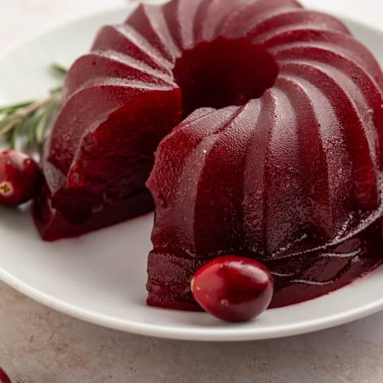 Jellied cranberry sauce made in a bundt pan on a white plate with a slice taken out of the side.
