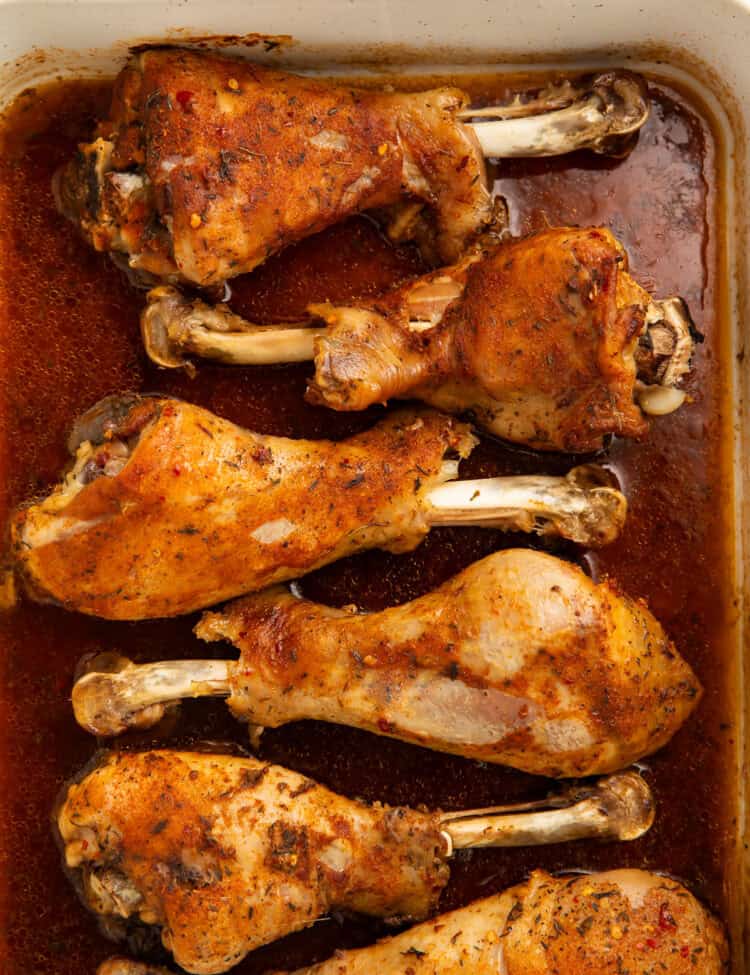 Six roasted turkey legs sitting in a pan gravy, covered in a spice rub.