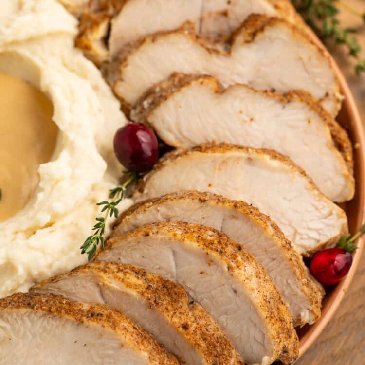 Sliced turkey tenderloin on a plate with mashed potato and gravy on the side.