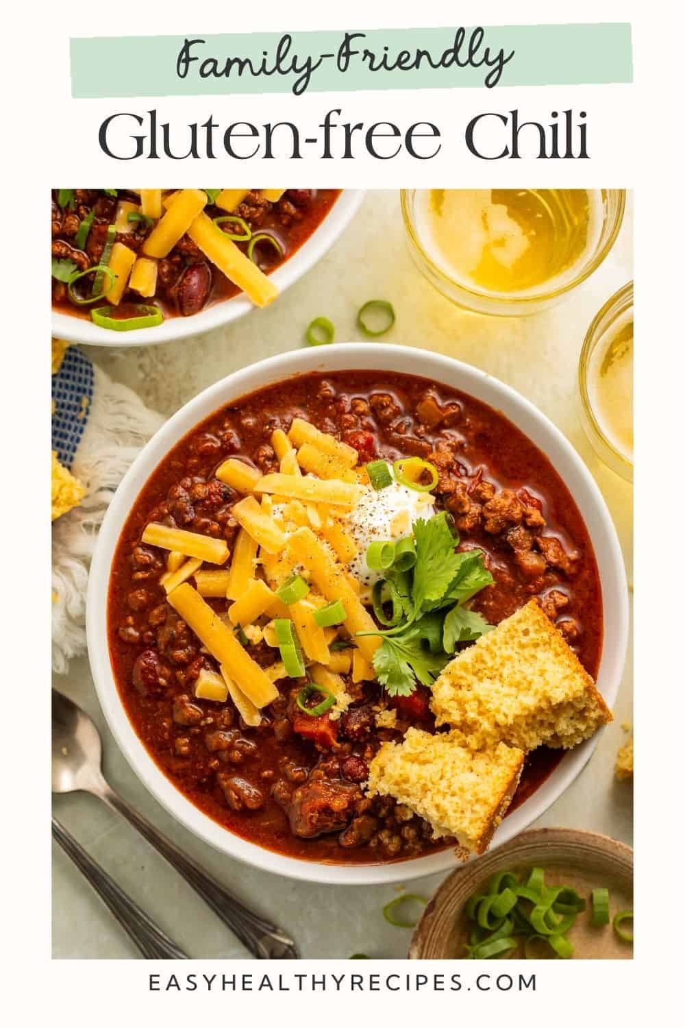 Close up of a bowl of chili topped with shredded cheese, sour cream, cilantro, green onion and crumbled cornbread with a Pinterest text overlay.