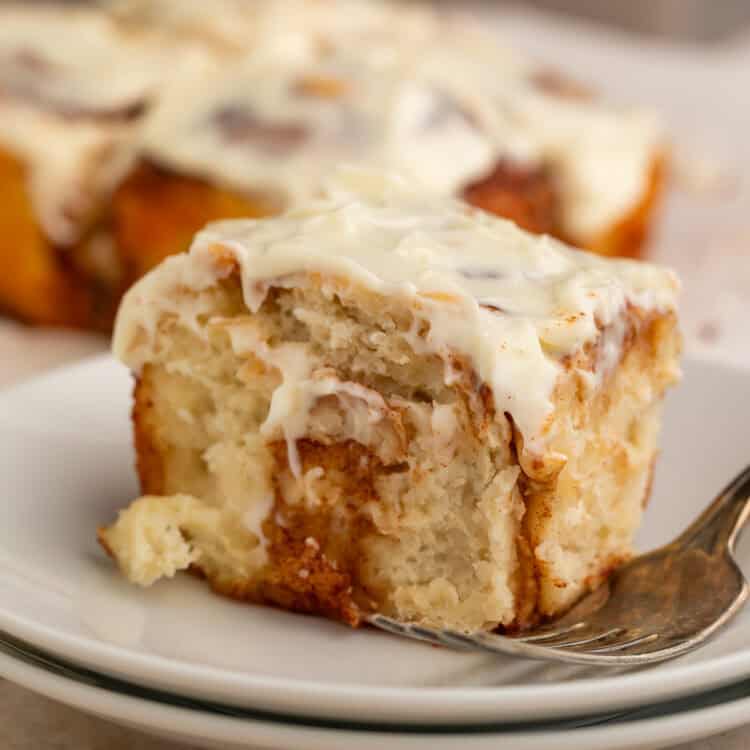 Frosted cinnamon roll on a stack of white plates with a fork.