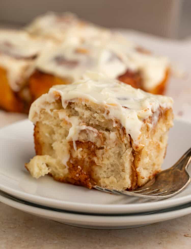 Frosted cinnamon roll on a stack of white plates with a fork.