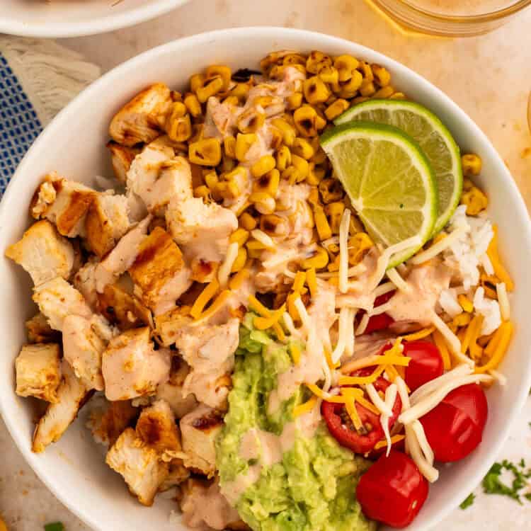 Close up of a taco bowl topped with diced chicken, charred corn, cherry tomatoes, guacamole and shredded cheese.