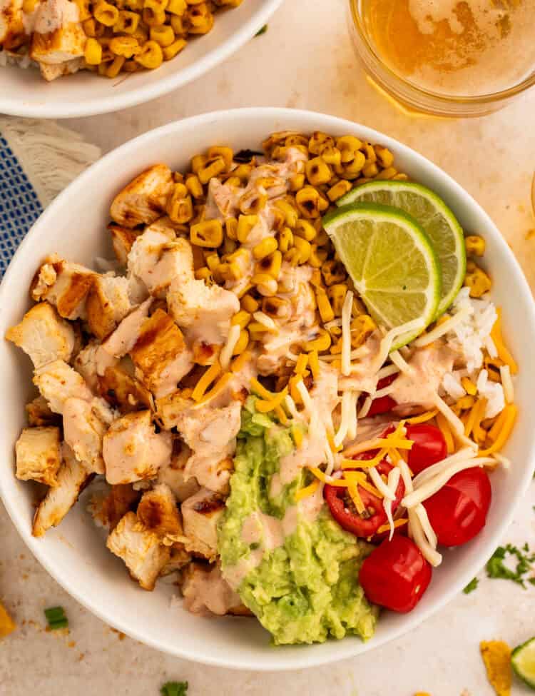 Close up of a taco bowl topped with diced chicken, charred corn, cherry tomatoes, guacamole and shredded cheese.