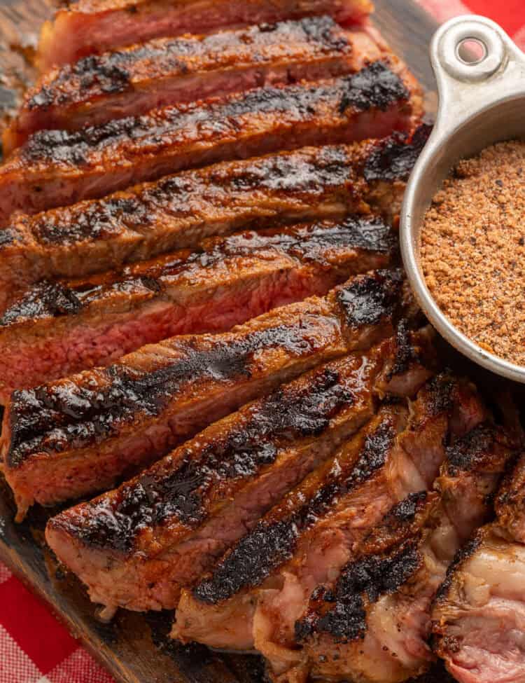 Close up of a sliced steak next to a metal measuring cup of steak seasoning.