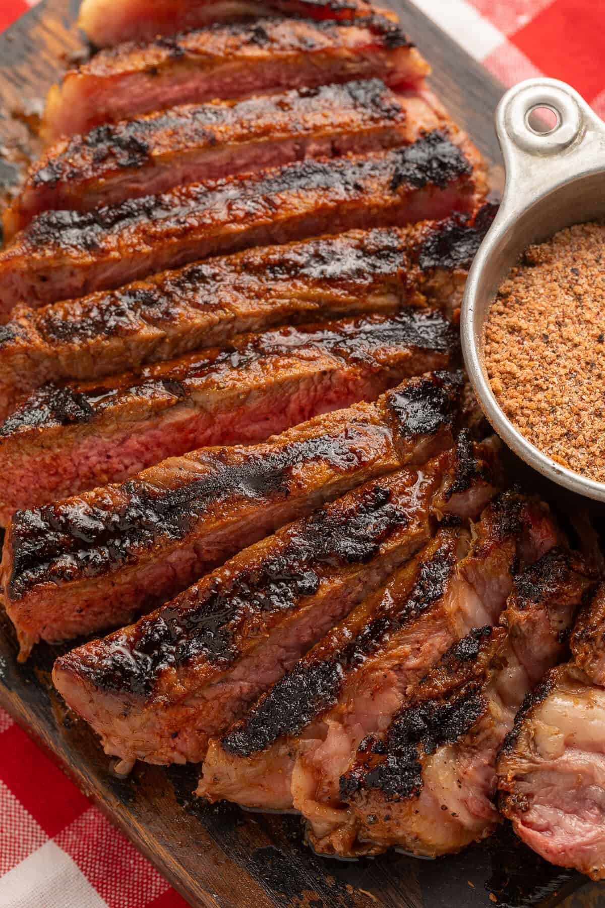 Close up of a sliced steak next to a metal measuring cup of steak seasoning.