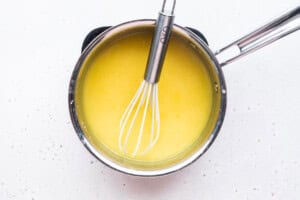 Overhead view of a small saucepan and whisk with bright yellow vegan lemon curd.