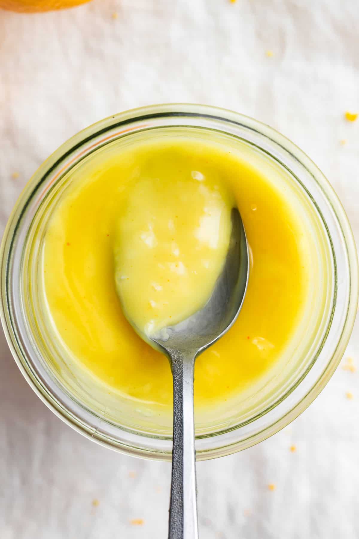 Overhead view of a jar of vegan lemon curd with a spoon.