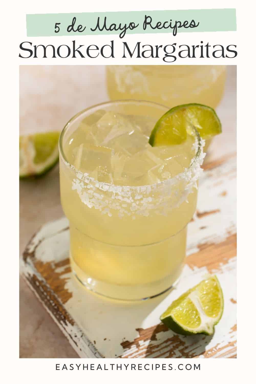 Close up of a margarita on the rocks in a salt rimmed glass with a lime wedge. There is another lime wedge on the board next to it. There is a white frame on the image with a Pinterest-optimised text overlay.