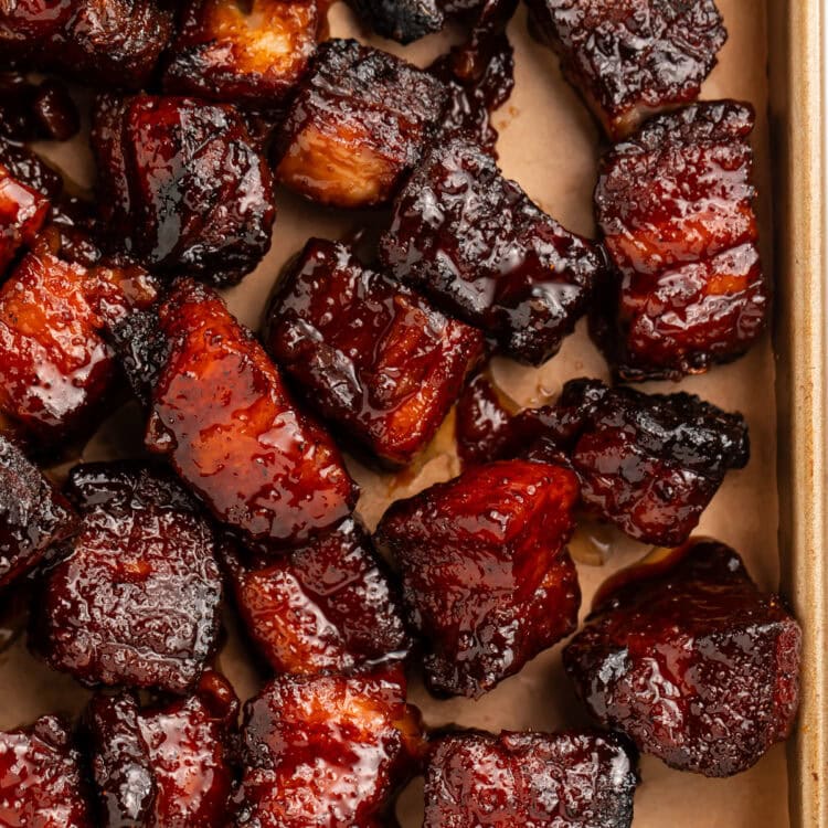 Close up of pork belly burnt ends on a lined baking sheet.