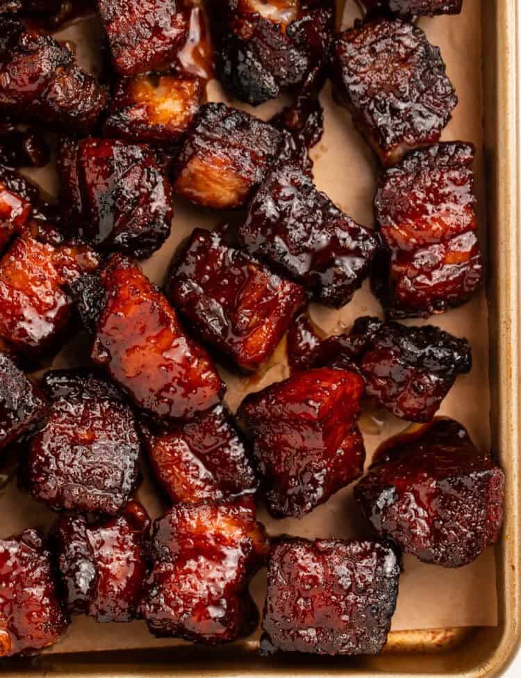 Close up of pork belly burnt ends on a lined baking sheet.