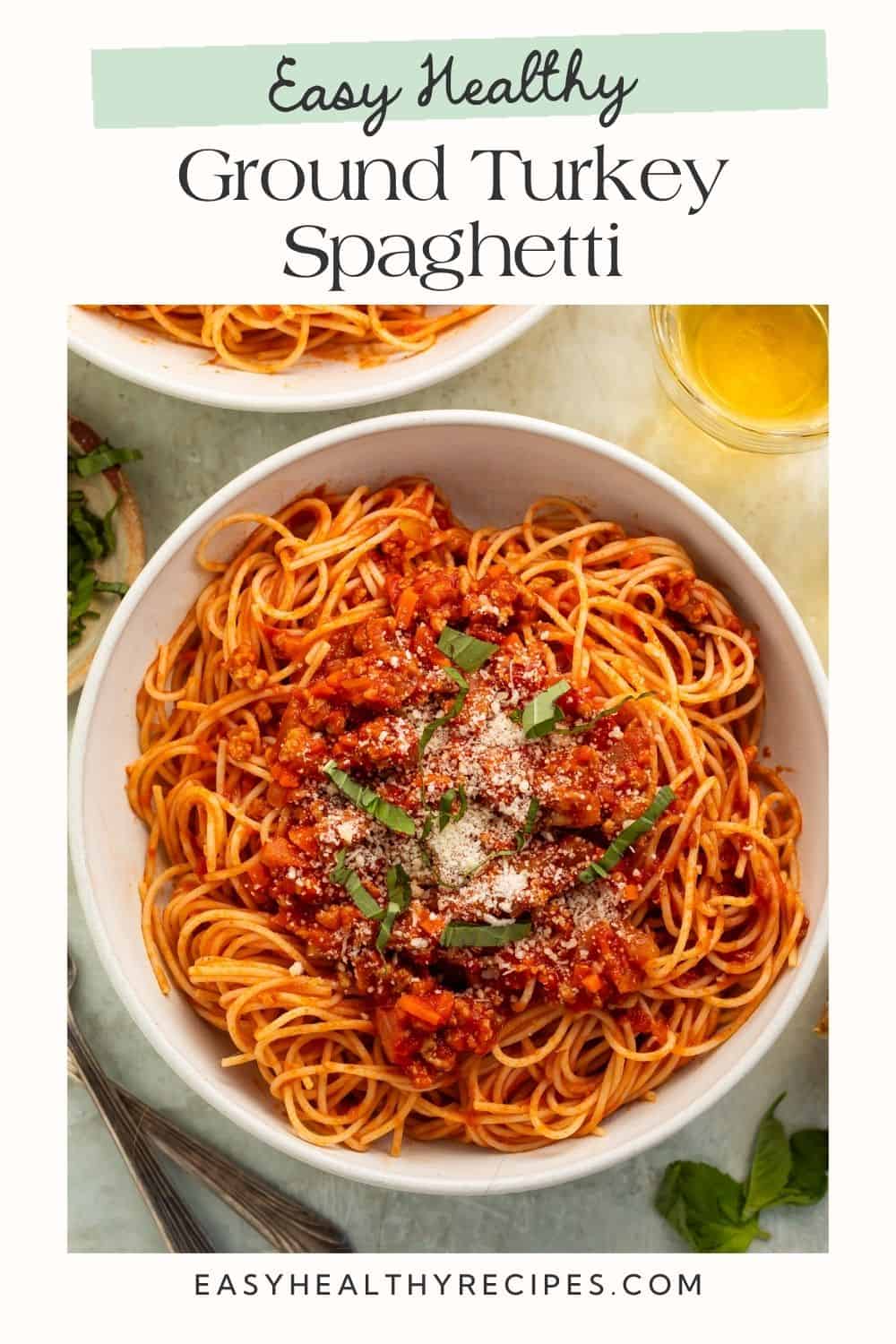 Bowl of ground turkey spaghetti topped with shredded parmesan and basil. There is a white frame on the image with a Pinterest-optimised text overlay.