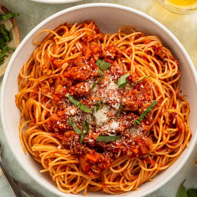 Bowl of spaghetti tossed in a ground turkey and tomato sauce topped with shredded basil and parmesan.