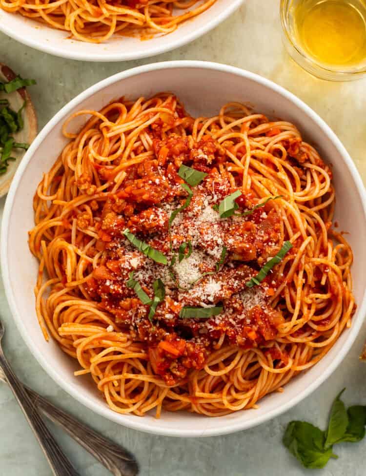 Bowl of spaghetti tossed in a ground turkey and tomato sauce topped with shredded basil and parmesan.