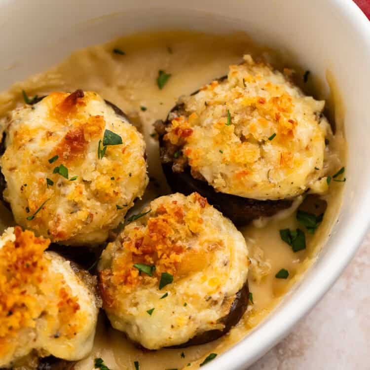 Close up of four baked mushrooms with crispy tops in a white baking dish.