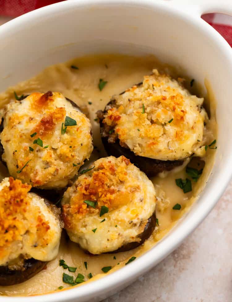 Close up of four baked mushrooms with crispy tops in a white baking dish.
