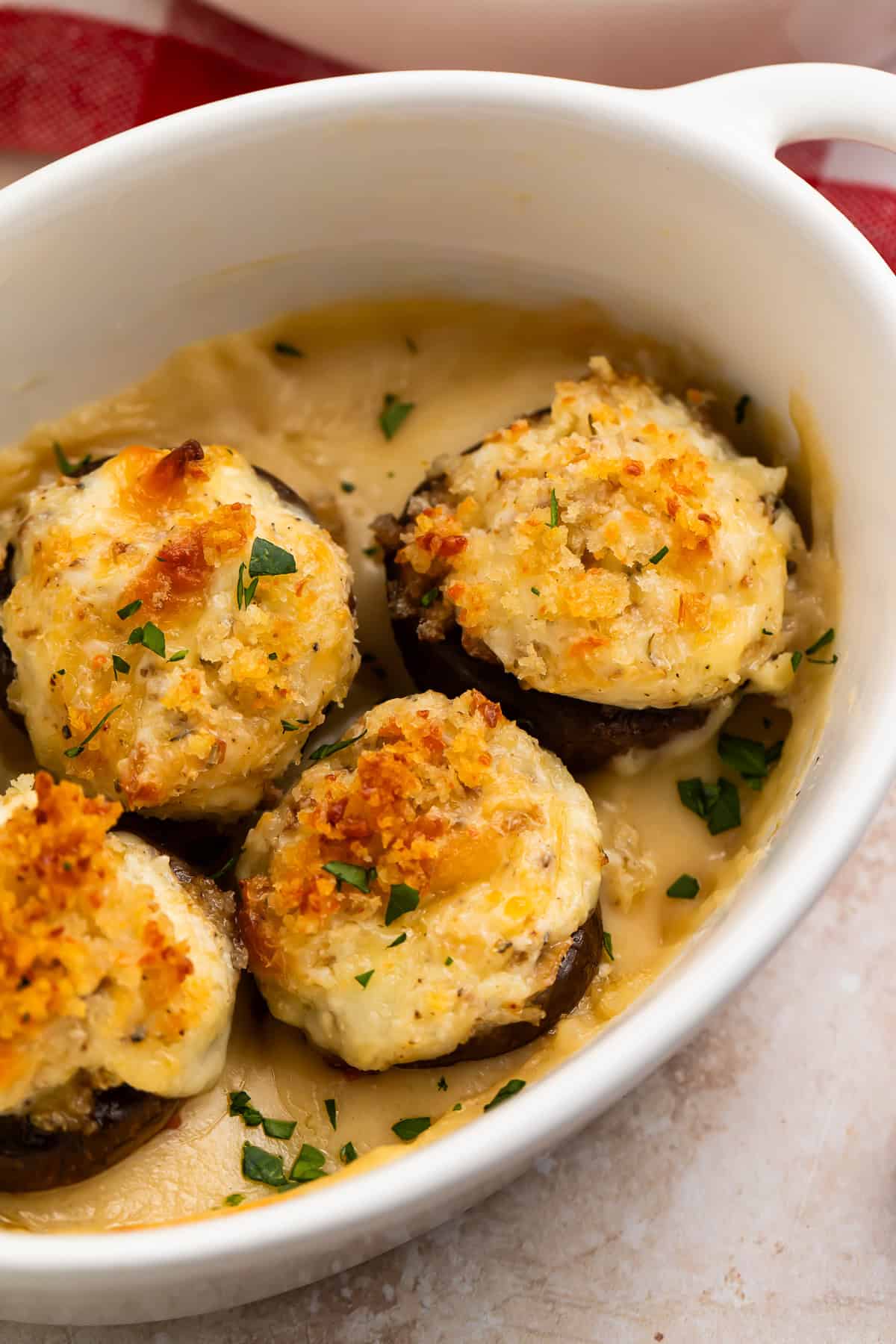 Close up of four baked mushrooms with crispy tops in a white baking dish.