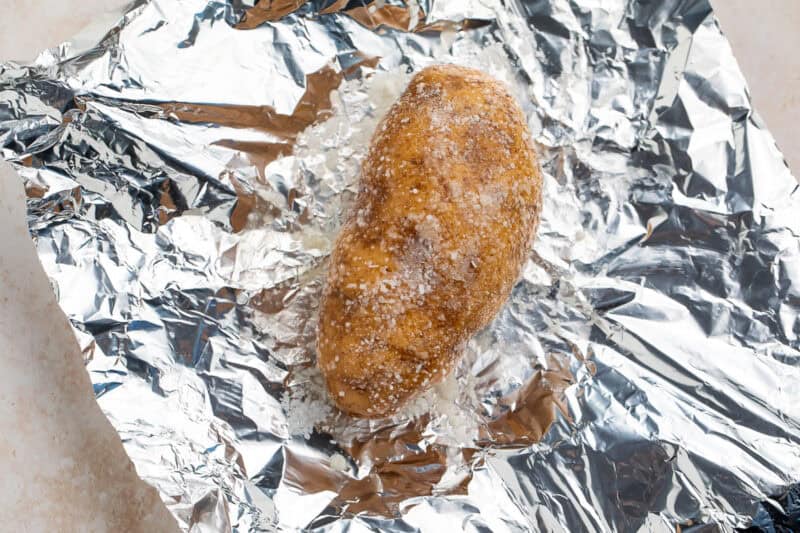 Baked potato with salt sitting in the middle of a piece of kitchen foil.