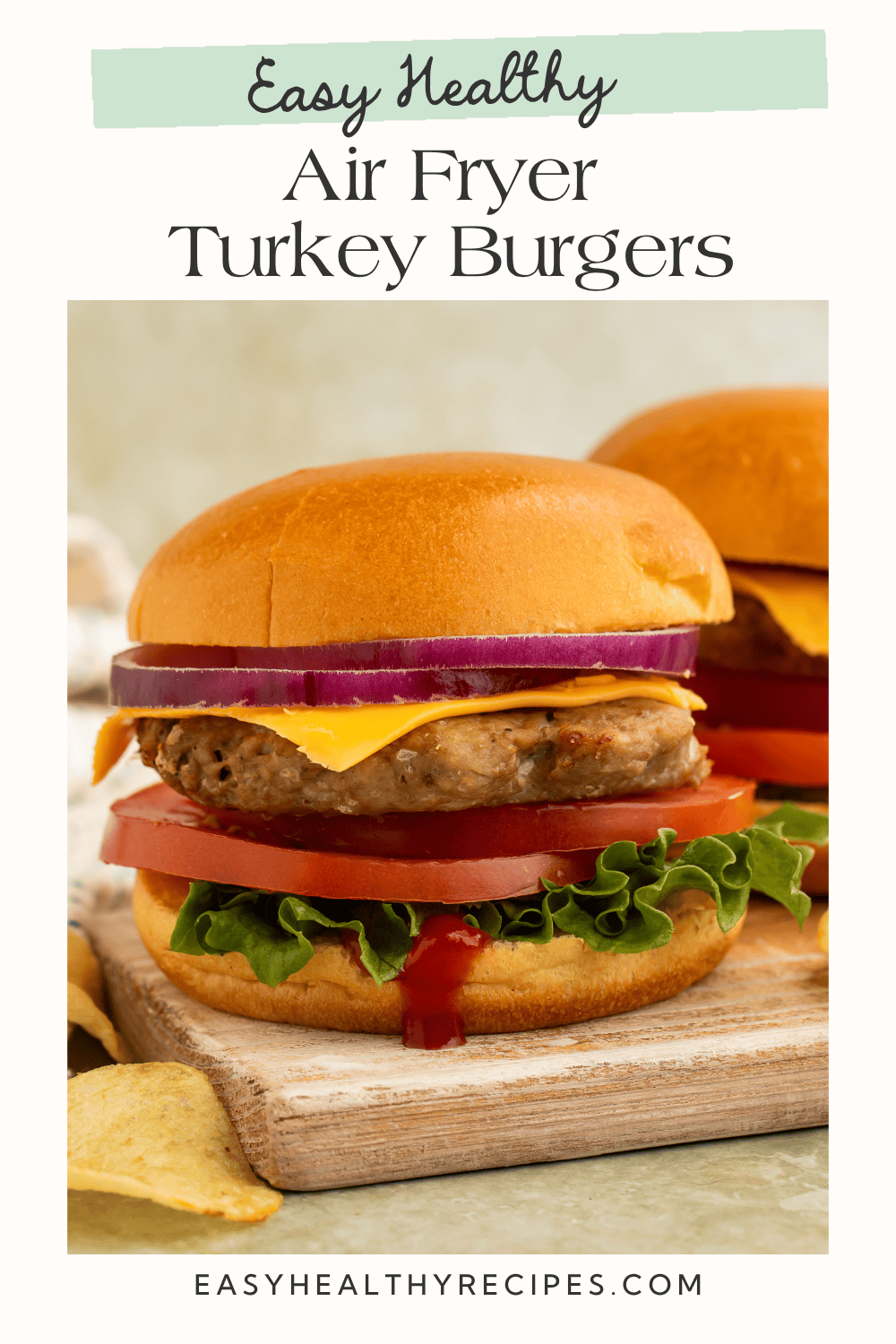 A juicy air fryer turkey burger stacked with cheddar cheese, red onion, tomato, and lettuce on a toasted bun, served on a wooden cutting board with potato chips