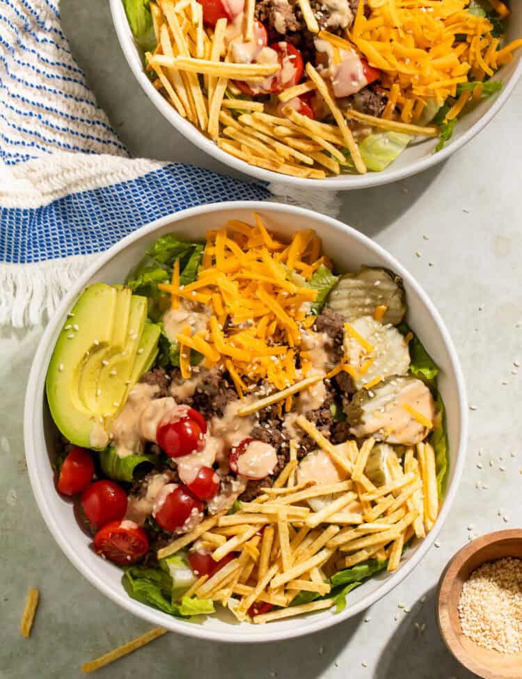 Burger bowls made with ground beef, lettuce, cheddar cheese, avocado, cherry tomatoes, pickles, crispy potato sticks, and burger sauce