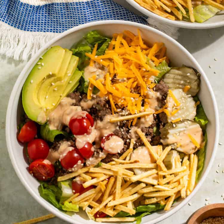 Close-up of a burger bowl with ground beef, cheddar cheese, avocado, pickles, tomatoes, and crispy potato sticks