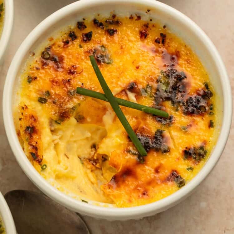 Close-up of baked crab brulee in a white ramekin with a golden caramelized topping and fresh chives