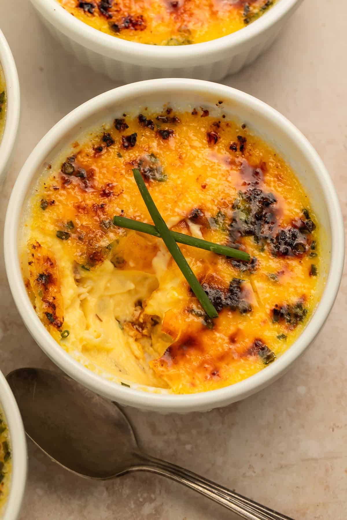Close-up of baked crab brulee in a white ramekin with a golden caramelized topping and fresh chives