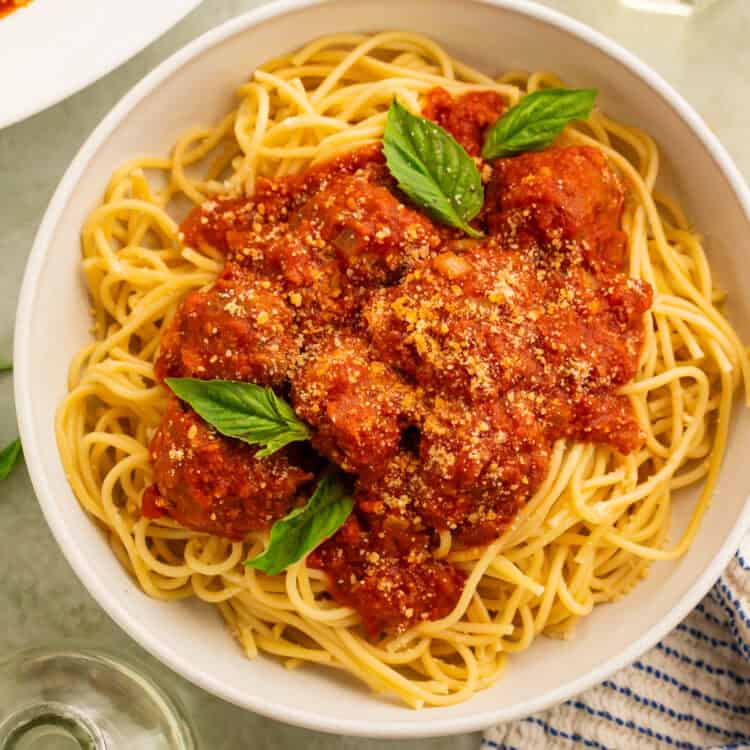 Gluten free meatballs in tomato sauce spooned over a bowl of spaghetti garnished with fresh basil leaves.