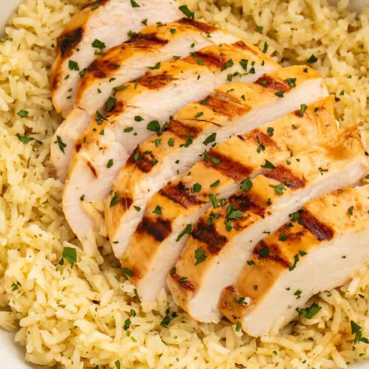 Close-up of sliced grilled chicken breast served over seasoned rice with parsley garnish