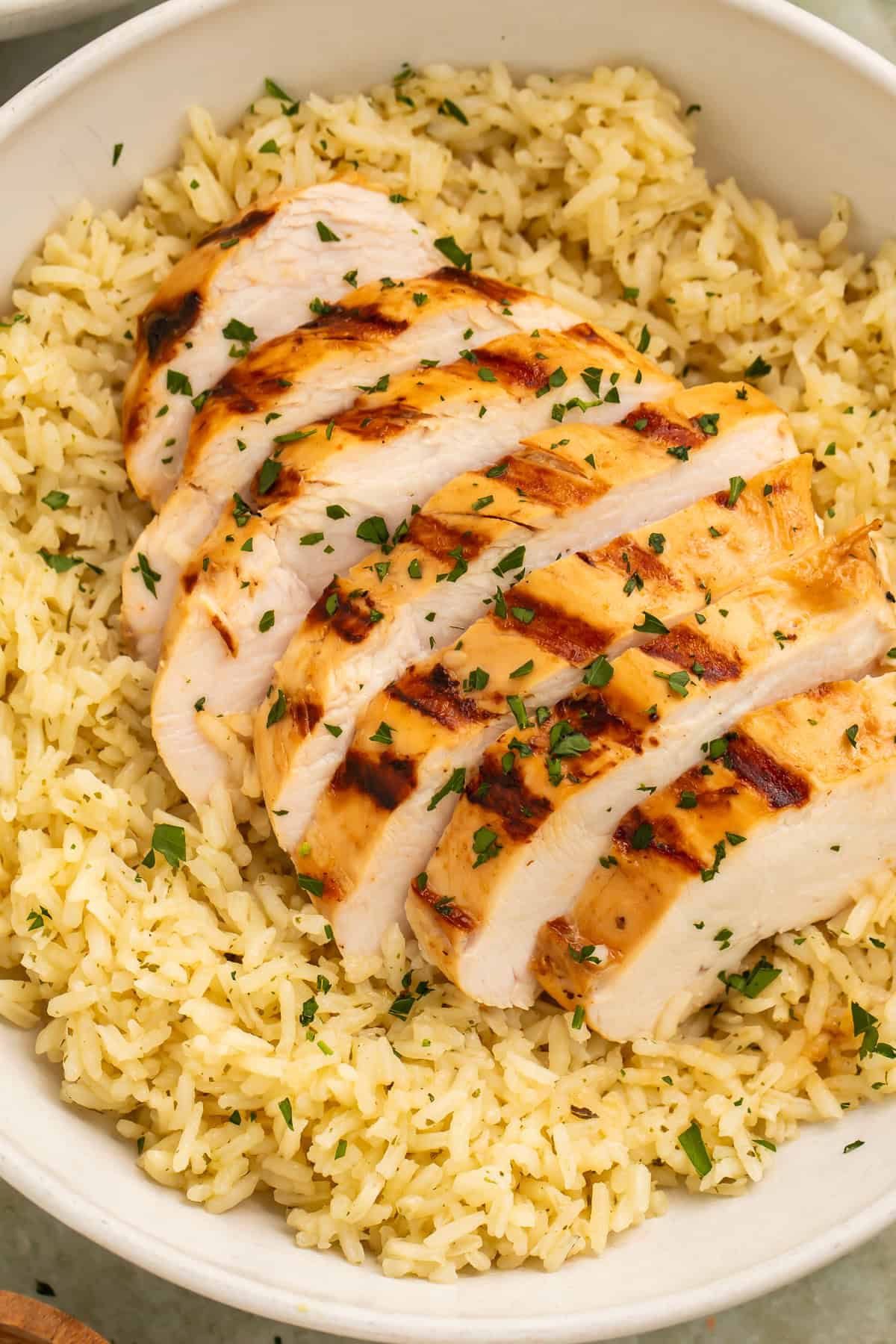 Close-up of sliced grilled chicken breast served over seasoned rice with parsley garnish