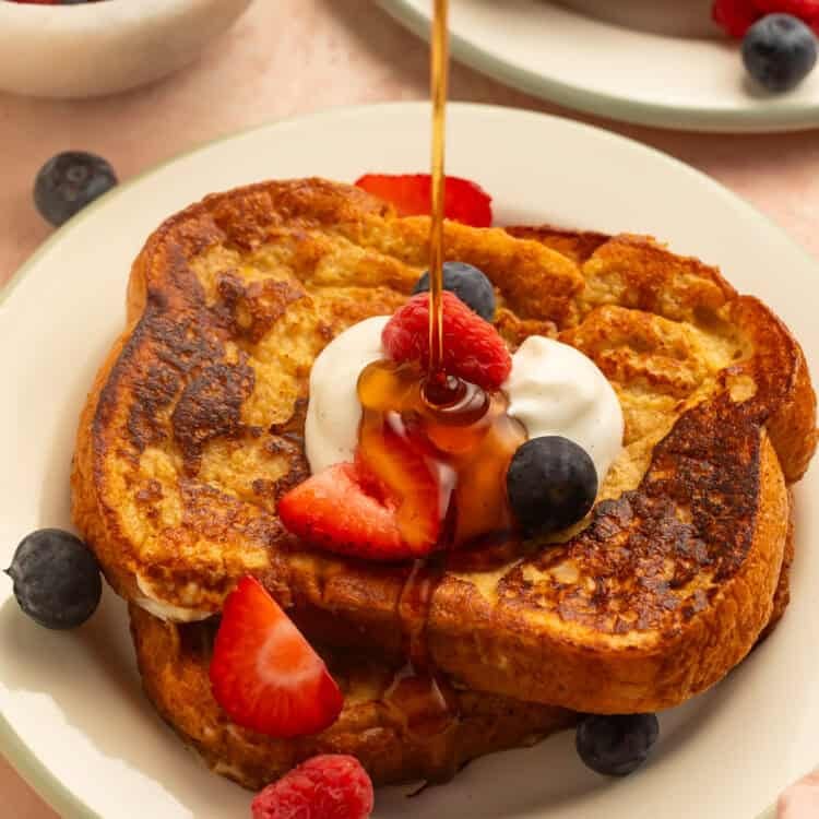 Healthy French toast topped with yogurt, strawberries, raspberries, and blueberries, drizzled with maple syrup