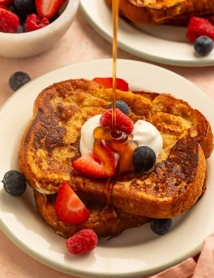 Healthy French toast topped with yogurt, strawberries, raspberries, and blueberries, drizzled with maple syrup