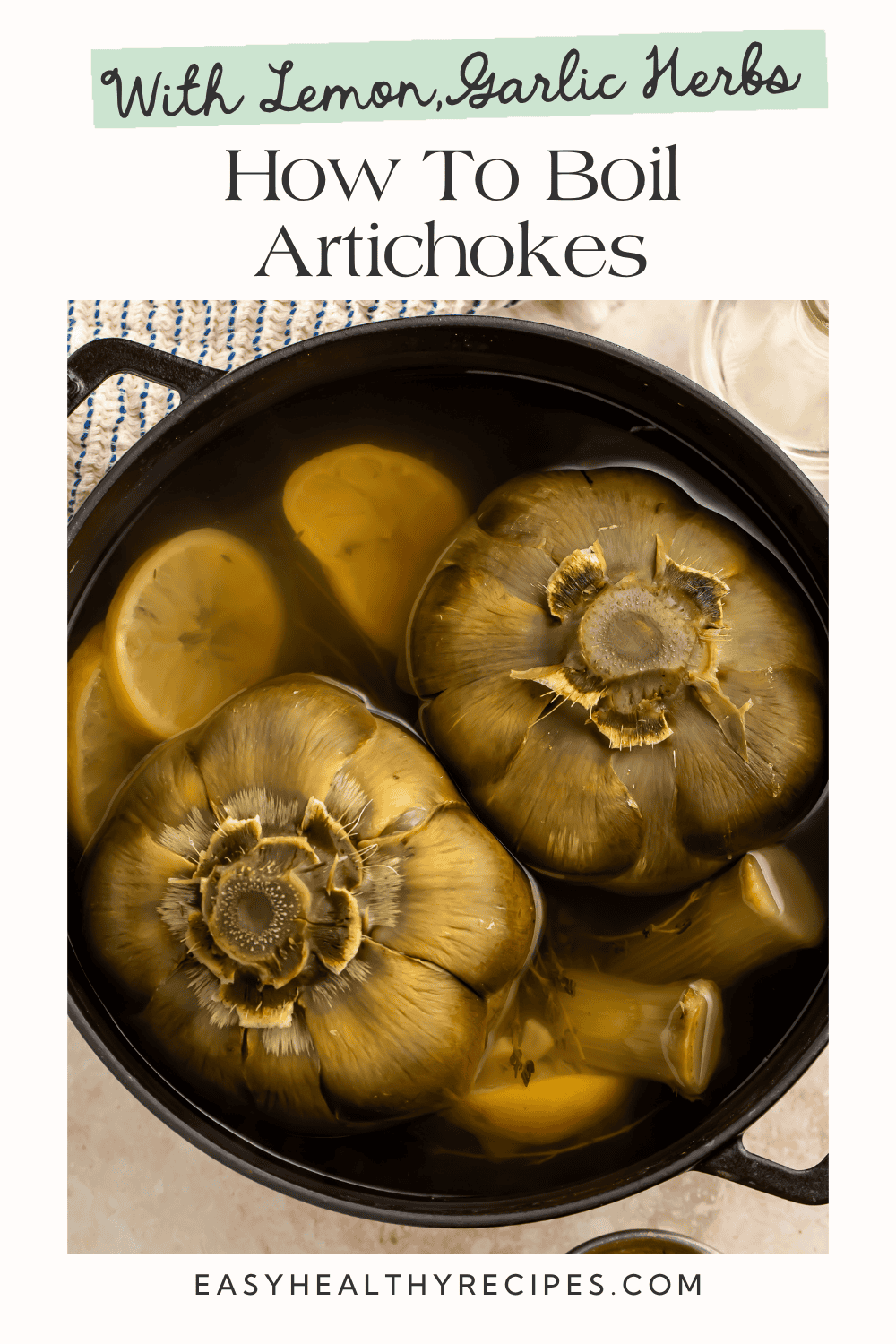 Two whole artichokes boiling in a black pot with lemon slices in herbed water
