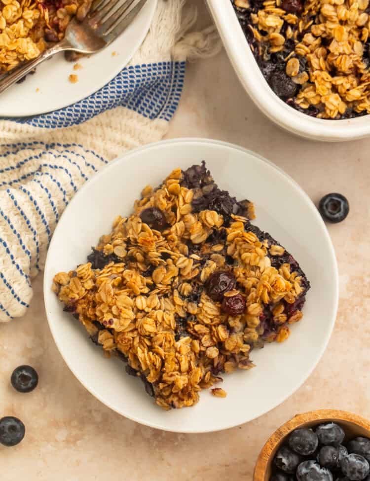 Blueberry baked oatmeal served in a bowl with fresh blueberries and a baking dish in the background