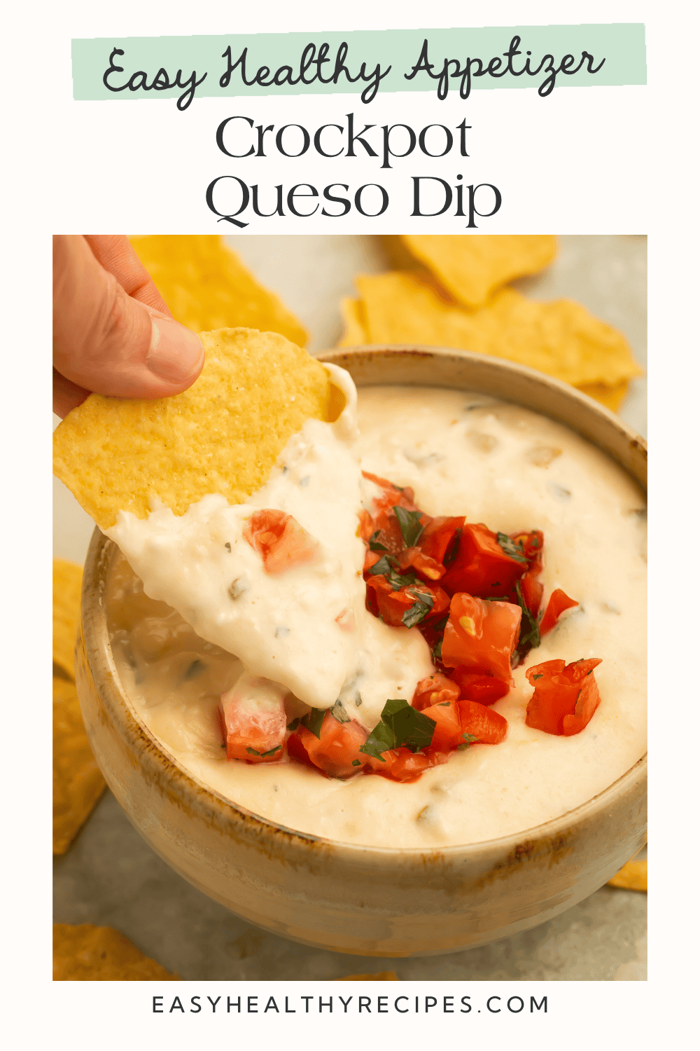 Tortilla chip being dipped into creamy crockpot queso dip topped with diced tomatoes and herbs